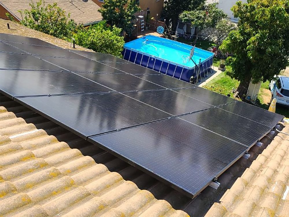 Black solar panels covering a tan concrete tile roof above a backyard pool